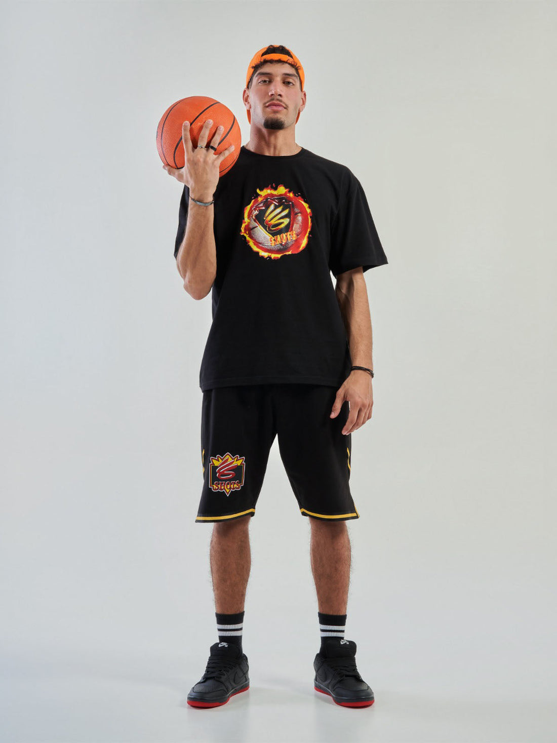 Person holding a basketball wearing a black t-shirt and shorts with a logo on a white background